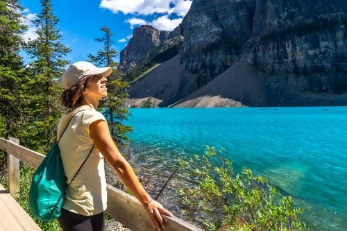 Hiker on the shore of turquoise Moraine Lake below steep cliffs