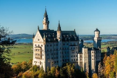 Neuschwanstein Castle with white towers above an autumn forest, lakes and open country behind