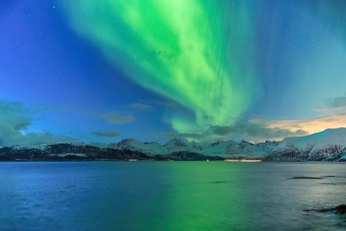 Green northern lights over snowy mountains and the sea