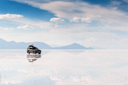 An off-road vehicle on the wet salt flat, which mirrors the sky and clouds